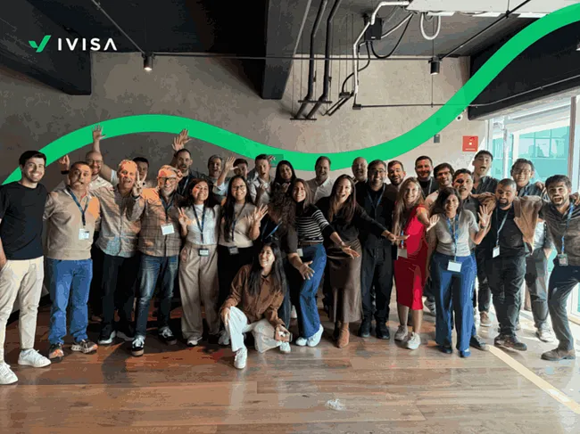 A large group of iVisa team members smiling and posing together in an office space, with the green iVisa wave logo in the background.